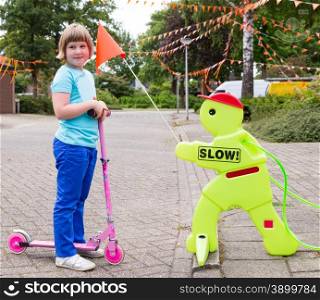 Young caucasian girl on pink scooter with safety figurine in street
