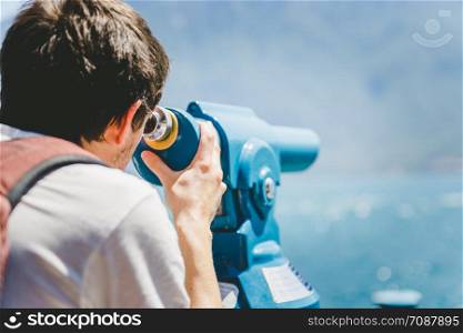 Young Caucasian man is looking through tourist binoculars, holiday