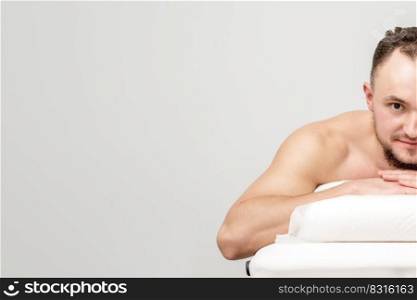 Young caucasian man lying on front on table spa, waiting for beauty treatment and looking at camera. Man lying on front on table spa