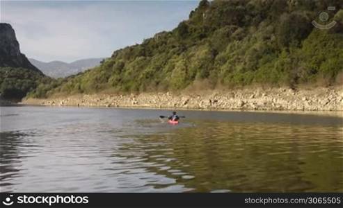 Young caucasian man on red canoe paddling on river during leisure activity
