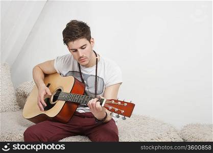 Young Caucasian man playing guitar while sitting on fur sofa