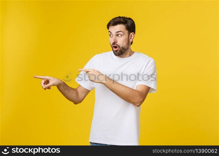 Young caucasian man pointing at something interesting on a yellow background.. Young caucasian man pointing at something interesting on a yellow background