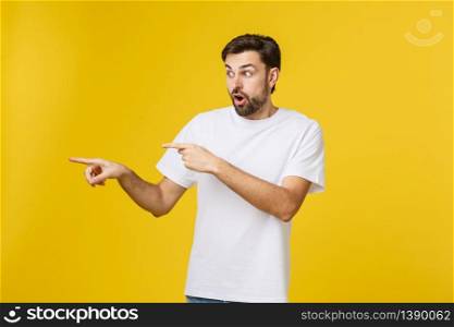 Young caucasian man pointing at something interesting on a yellow background.. Young caucasian man pointing at something interesting on a yellow background