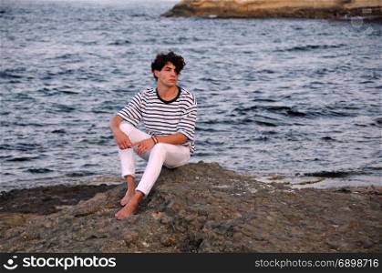Young Caucasian man sits on the rock in the Black sea