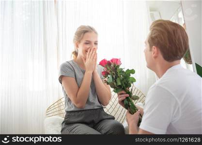 Young caucasian man surprise girlfriend with bunch of rose to celebrate their anniversary wedding day.couple have happy time together in home .Valentine day concept.