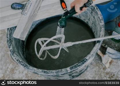 Young caucasian man unrecognizable washes from putty a construction mixer in a black basin under a shower net, close-up top view with selective focus. The concept of home renovation, construction work.. A young man washes a construction mixer.