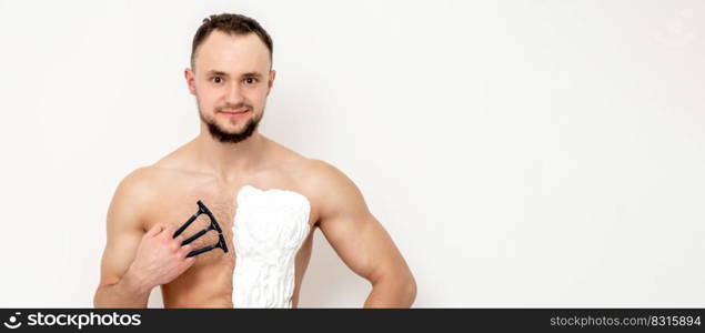 Young caucasian man with beard holds razor shaves his chest with white shaving foam on white background. Man shaving his torso. Young man shaving his chest