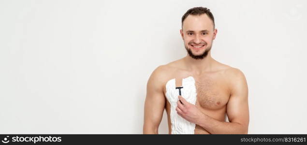 Young caucasian man with beard holds razor shaves his chest with white shaving foam on white background. Man shaving his torso. Young man shaving his chest