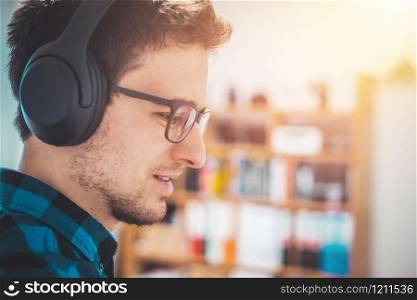 Young Caucasian man with checked blue shirt is listing to music with wireless headphones