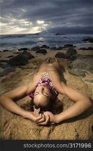 Young Caucasian nude woman wearing lei lying on beach in Maui, Hawaii, USA.