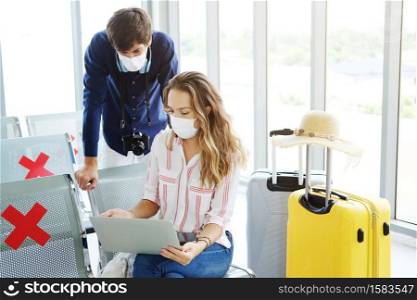 Young Caucasian traveler couple love wear mask for prevention for covid-19 virus is relaxing with laptop for online social media together in the airport. Healthcare for Honeymoon trip on vacation.