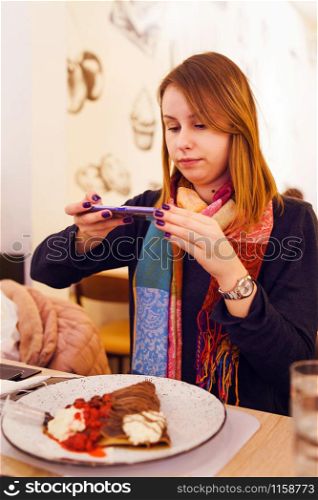 Young caucasian woman at the restaurant taking photo of the sweet food pancake with her mobile smart phone
