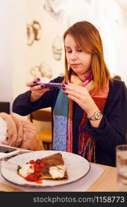 Young caucasian woman at the restaurant taking photo of the sweet food pancake with her mobile smart phone