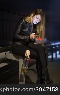 Young caucasian woman drinking alcohol and typing message on street at night