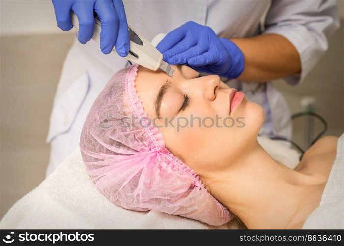 Young caucasian woman having ultrasonic peeling with ultrasound device in a cosmetic beauty salon. Young caucasian woman having ultrasonic peeling with ultrasound device in a cosmetic beauty salon.