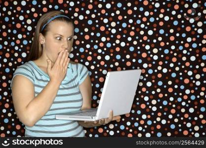 Young Caucasian woman holding laptop looking shocked.