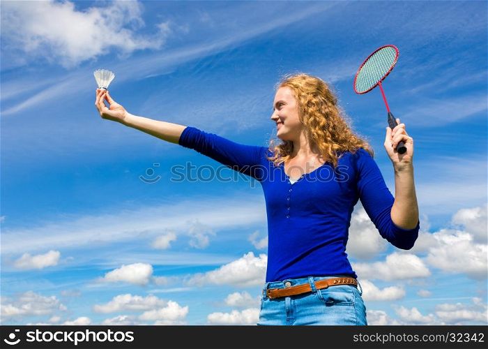 Young caucasian woman holding shuttle and badminton racket against blue sky with white clouds