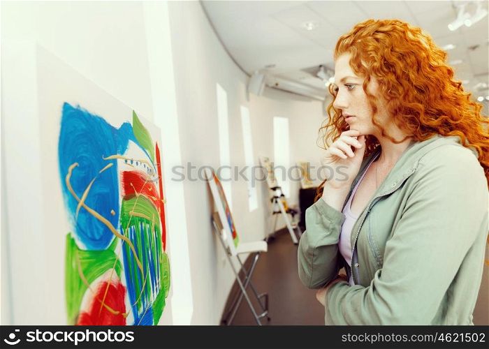 Young caucasian woman in art gallery front of paintings. Young caucasian woman in an art gallery in front of painting displayed on white wall