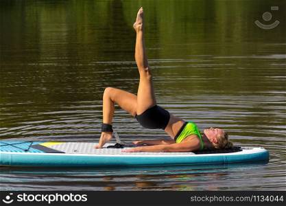 Young caucasian woman in yoga posture with leg up on paddle board