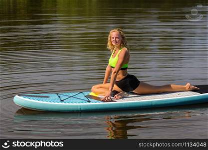 Young caucasian woman in yoga swan position on paddle board at water