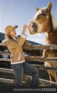 Young Caucasian woman leaning on fence petting horse.