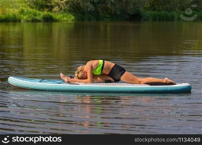 Young caucasian woman lying in splits on paddle board in water