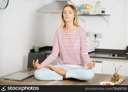 Young caucasian woman meditating in the kitchen at home. Young blonde woman meditating in the kitchen at home