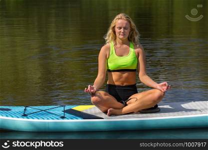 Young caucasian woman meditating on SUP in dutch river
