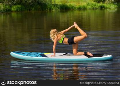 Young caucasian woman on SUP in yoaga pose on river