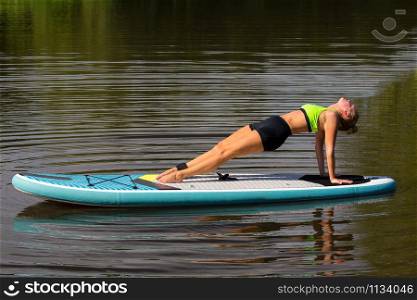 Young caucasian woman planking backward on paddle board at lake