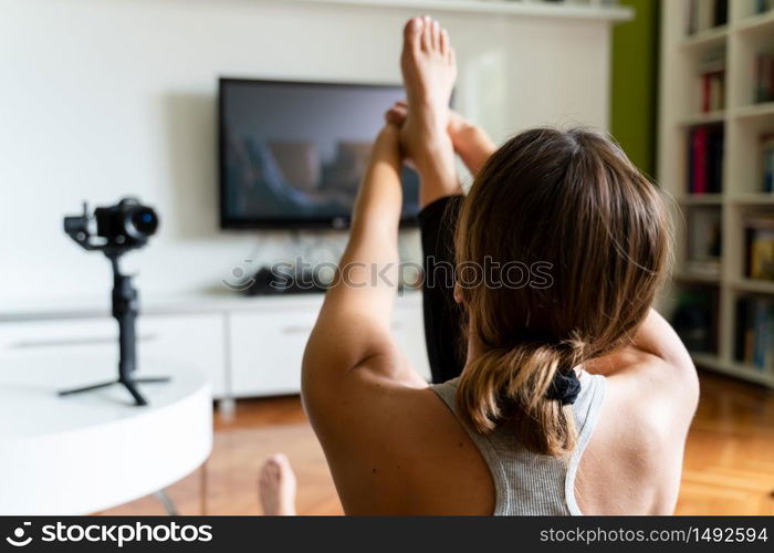 Young caucasian woman practicing yoga at home beautiful instructor teaching online class training in the apartment talking in front of camera and laptop making video blog or vlog back view