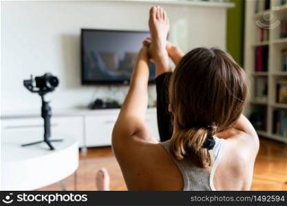 Young caucasian woman practicing yoga at home beautiful instructor teaching online class training in the apartment talking in front of camera and laptop making video blog or vlog back view