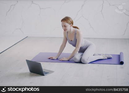 Young caucasian woman practicing yoga on mat on floor of her room. Internet fitness lesson with computer on self isolation. Concept of e-learning and home online classes on corona virus quarantine.. Young woman practicing yoga internet fitness lesson on self isolation. Home online classes.