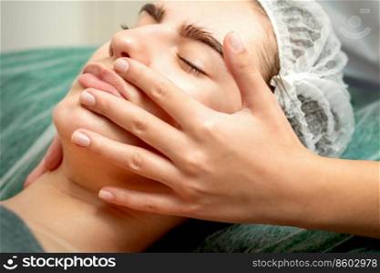Young caucasian woman receiving facial massage by beautician&rsquo;s hands in spa medical salon. Young woman receiving facial massage