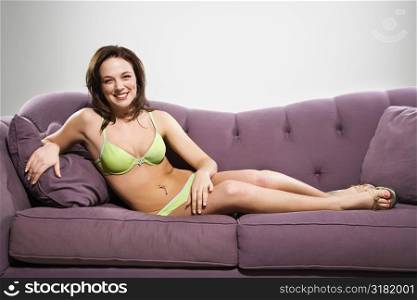 Young Caucasian woman reclining on couch in lingerie smiling at viewer.