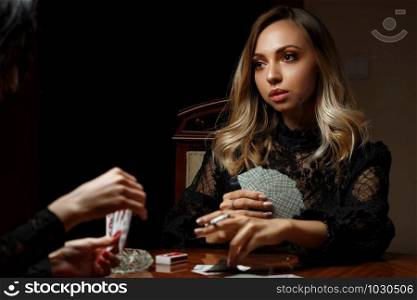 young caucasian woman sits at a table, plays cards for undressing and smokes