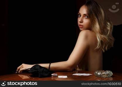 young caucasian woman sits at table with bare breasts after losing cards