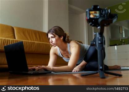 Young caucasian woman sitting at home beautiful instructor teaching online yoga class training in the apartment in pose asana in front of camera and laptop making video blog or vlog in day or morning