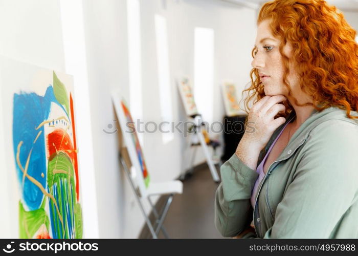 Young caucasian woman standing in art gallery front of paintings. Young caucasian woman standing in an art gallery in front of painting displayed on white wall