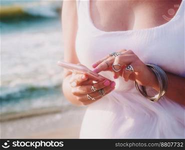 Young caucasian woman using smartphone by the sea. Only hands with boho gypsy jewelry. Slow motion. Technology concept.