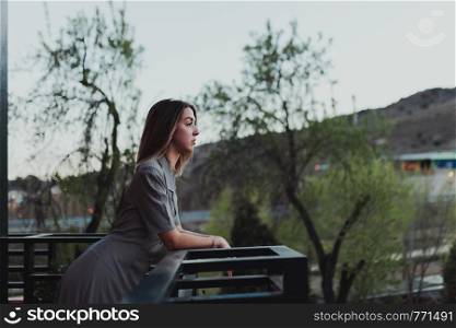 Young caucasian woman watch the sunset from her balcony.
