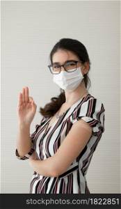 Young Caucasian woman wear face mask and glasses smile and showing plaster stuck on arm to show that she get vaccinated with hand make okay sign