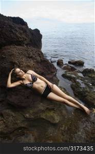 Young Caucasian woman wearing bathing suit lying down on rocky beach in Hawaii.