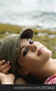 Young Caucasian woman wearing hat lying down with hands behind head.