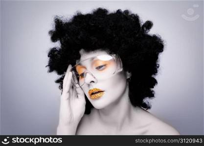 Young caucasian woman with gold fashion makeup and gold diamonties on her lips wearing a black afro wig. Young caucasian woman with gold fashion makeup