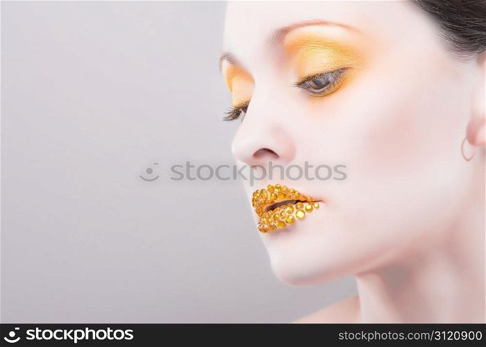 Young caucasian woman with gold fashion makeup and gold diamonties on her lips. Young caucasian woman with gold fashion makeup