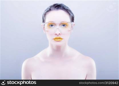 Young caucasian woman with gold fashion makeup wearing clear glasses and gold diamonties on her lips. Young caucasian woman with gold fashion makeup