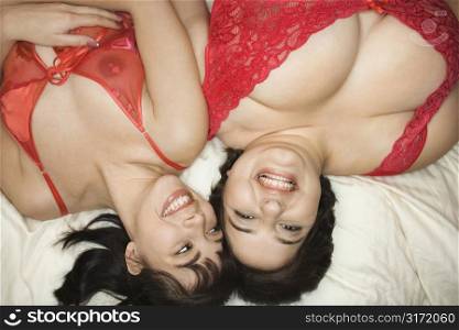 Young Caucasian women in sexy red lingerie lying in bed smiling.
