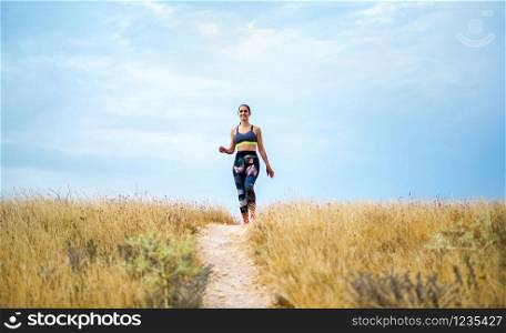 Young caucassian sportswoman running on the countryside exercising on summer. Young women running over the top of a dirt trail in mountains on summer