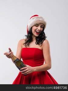 Young celebrating woman christmas santa hat and dress. Beautiful model portrait isolated over studio background opening champagne bottle.